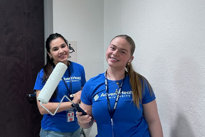 Two students smiling and painting for all AHU service day