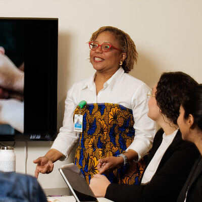 A faculty member stands in front of a monitor and lectures to a small group of students